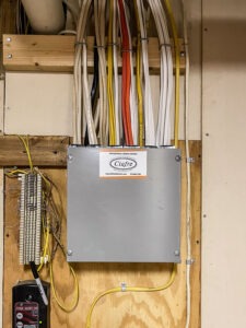 An electrical panel with multiple colored cables organized above it on a wooden board. There's a small device with a 'Gas Alert' label on the left. The panel has a label reading "Ciafre", indicating electrical services.